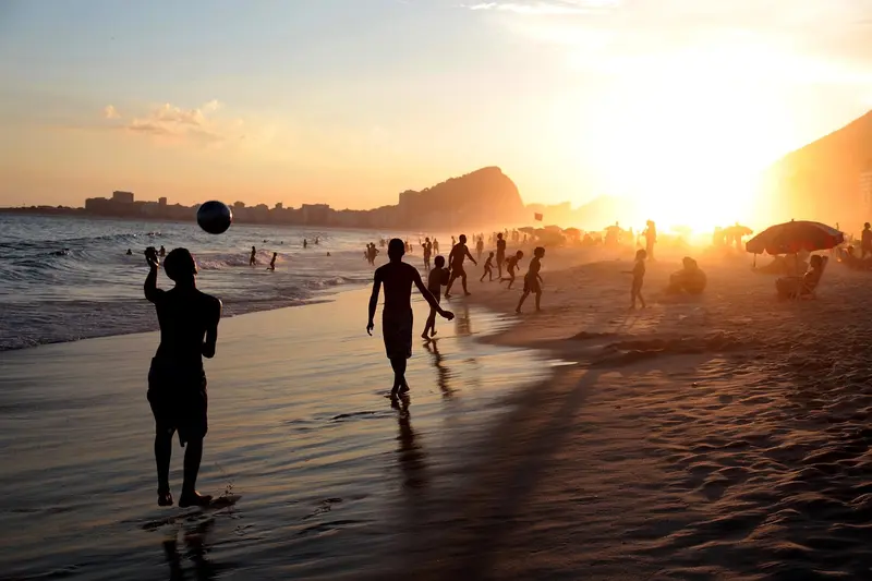 Amigos jogando bola na praia ao pôr do sol